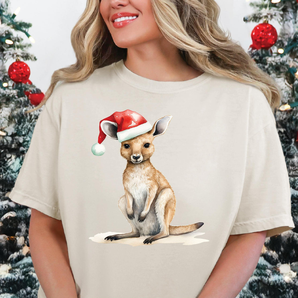 A person wearing a beige t-shirt with a graphic print of a kangaroo wearing a Santa hat, surrounded by Christmas decorations.