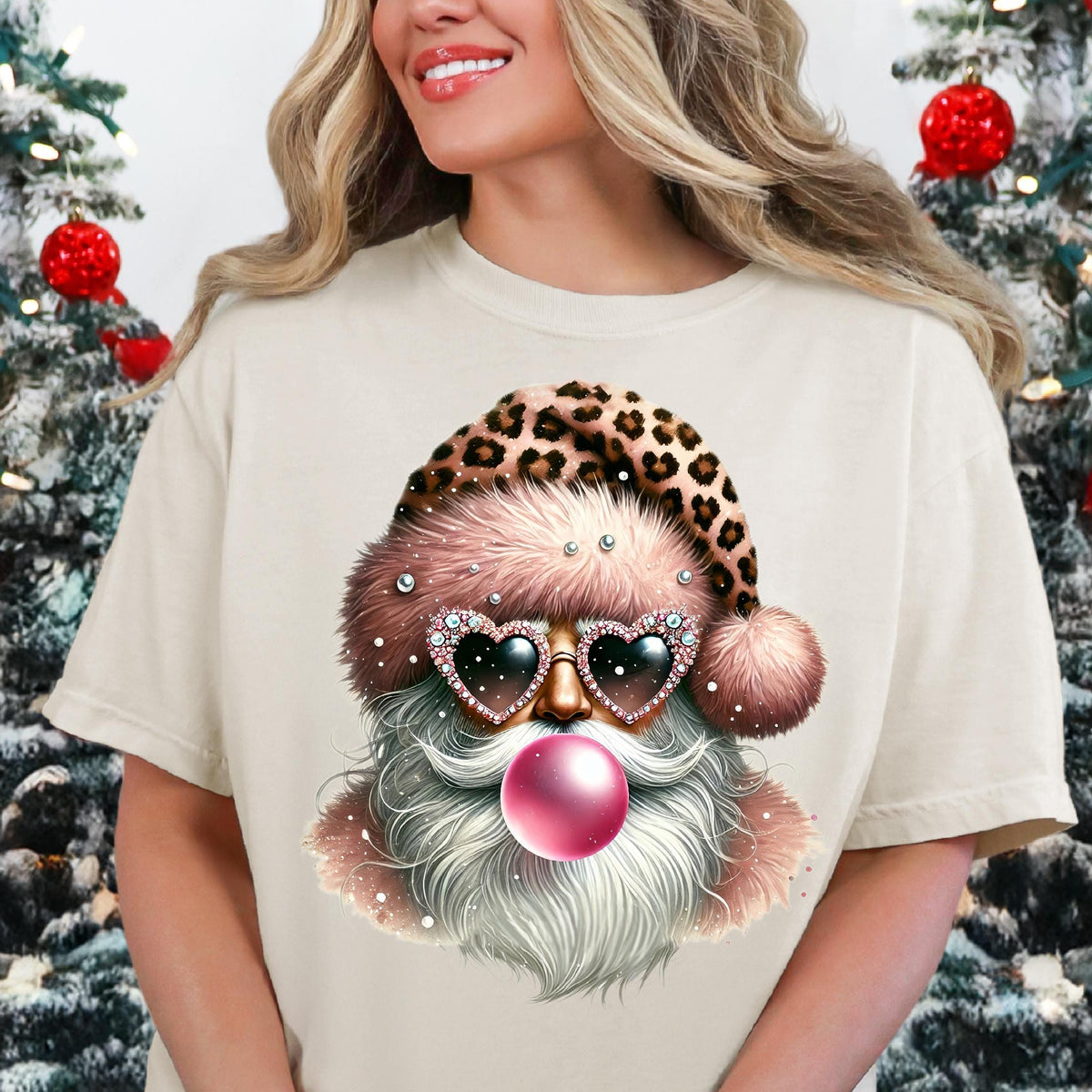 A person wearing a beige t-shirt with a retro Santa Claus design, featuring sunglasses and a pink bubble, against a Christmas-themed background with a tree and gifts.
