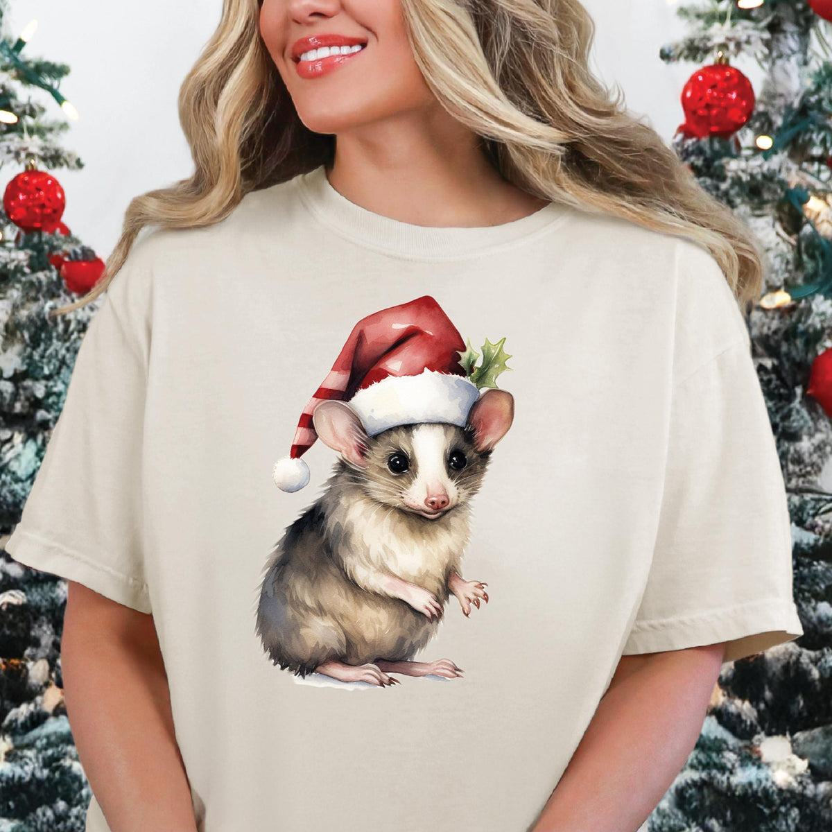 A person wearing a beige t-shirt with a graphic print of a koala wearing a Santa hat, surrounded by Christmas decorations.