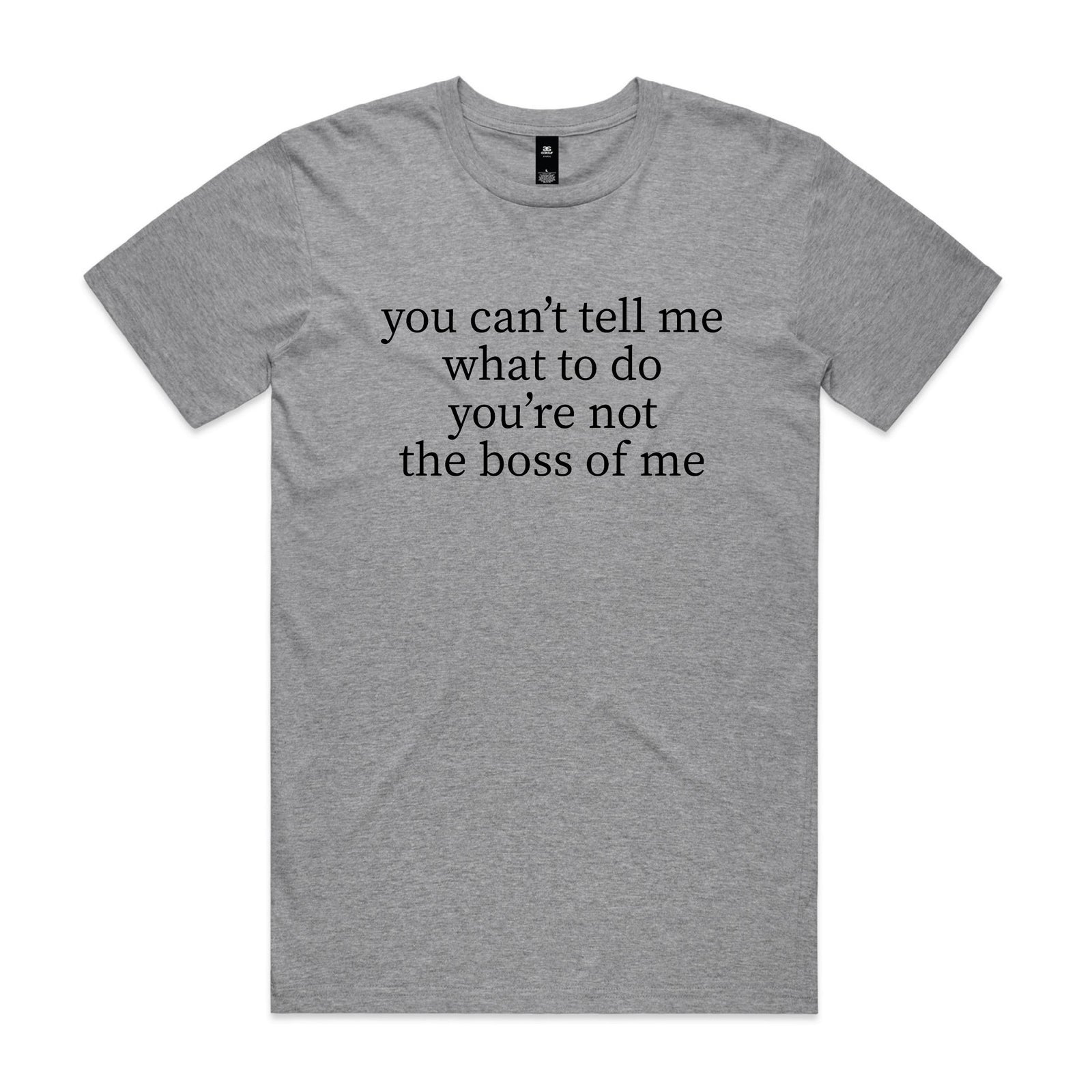 Smiling older man with crossed arms standing in a backyard, wearing a grey marle t-shirt with black serif text reading you can't tell me what to do you're not the boss of me.