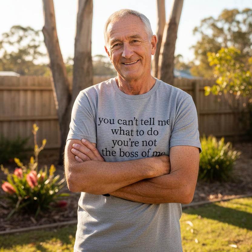 Smiling grandad in a backyard wearing a grey You Can't Tell Me What To Do You're Not The Boss Of Me t-shirt with bold serif lettering