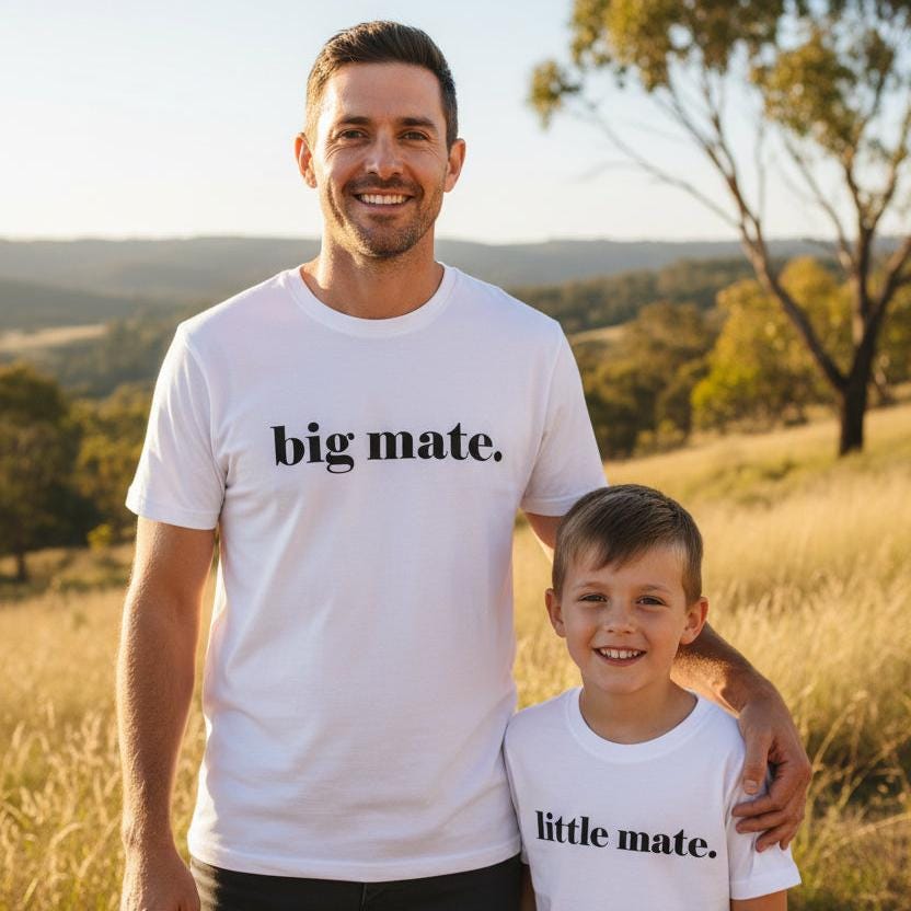 Tilly&Wilbur white matching set — an adult tee printed with "big mate." and a baby bodysuit printed with "little mate." in minimalist black lowercase text, worn by a dad standing with his son outdoors