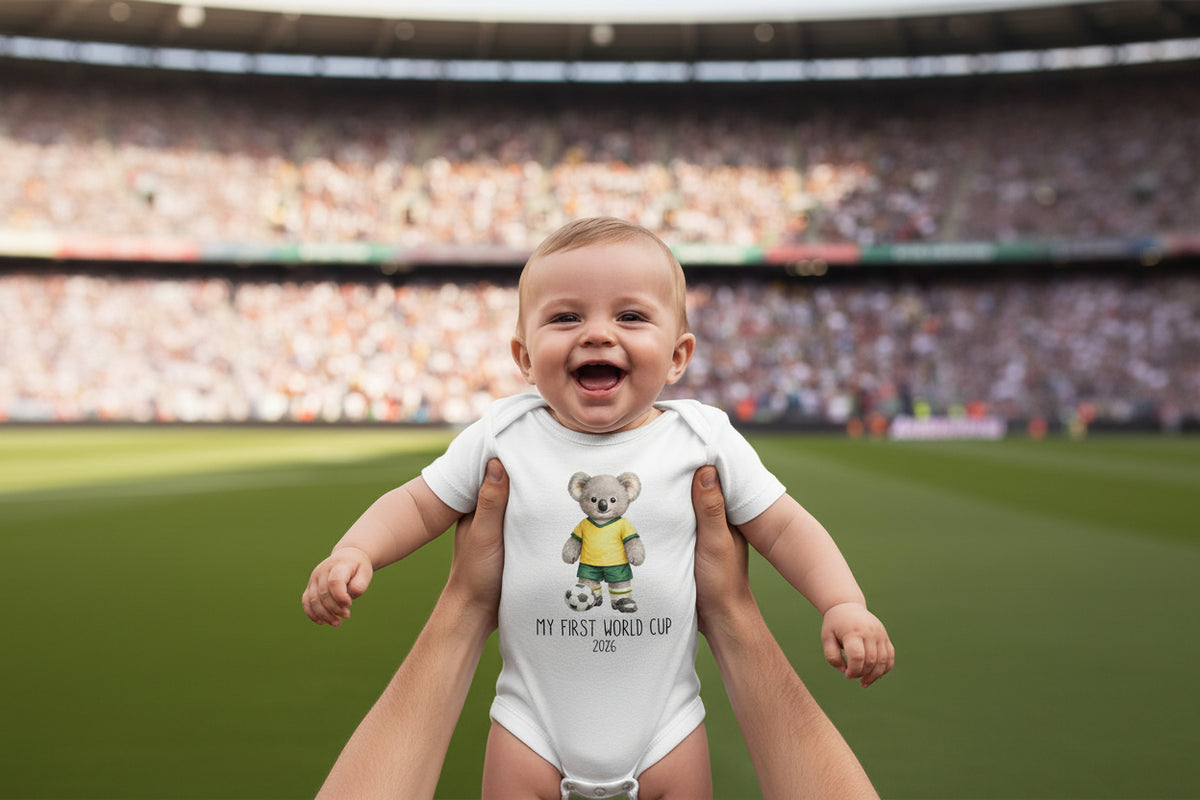 Tilly&amp;Wilbur white baby bodysuit printed with a green and gold koala soccer player and &amp;quot;My First World Cup&amp;quot; with a personalised year, held up at a stadium.