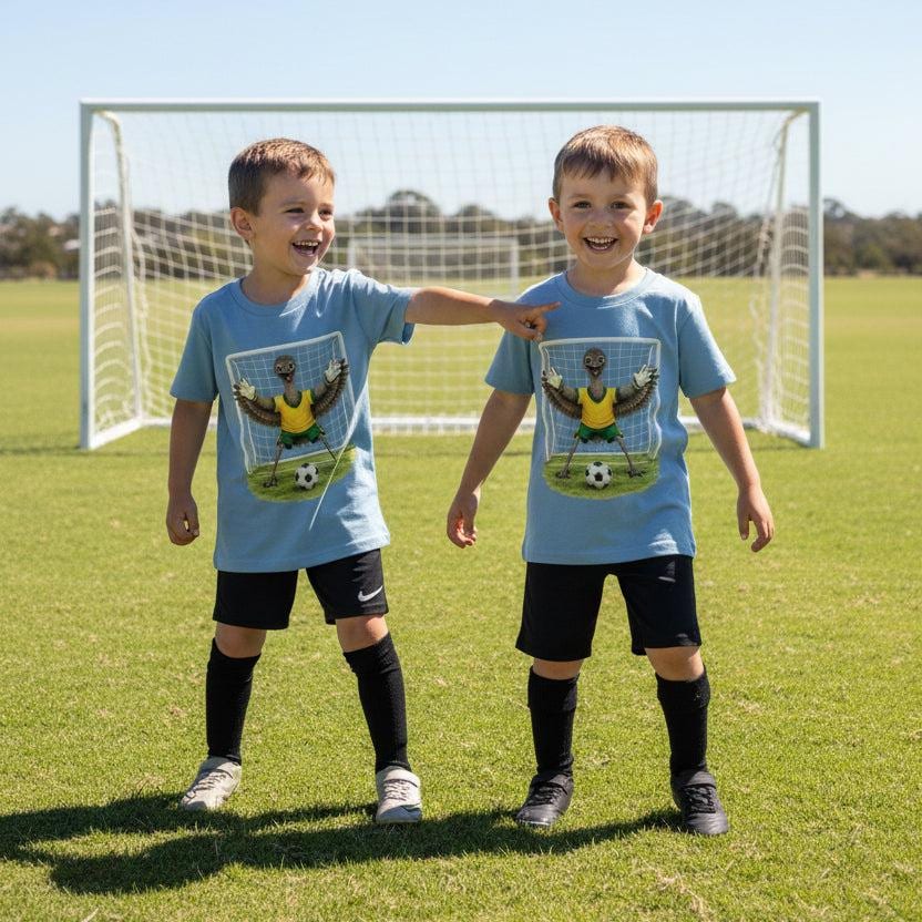 Tilly&Wilbur light blue kids tees printed with an illustrated emu goalkeeper in a green and gold soccer kit, worn by two young boys standing in a soccer goal