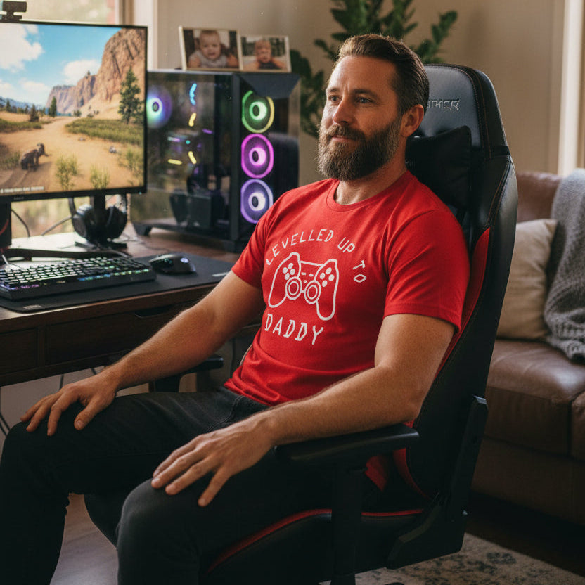 A red short-sleeve crewneck t-shirt with a white graphic print on the front. The graphic features the text 'LEVELLED UP TO DADDY' surrounding a video game controller illustration.