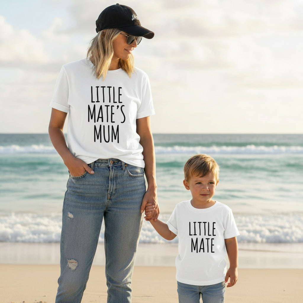 Mother and child wearing matching black Little Mate’s Mum and Little Mate shirts, walking together on the beach