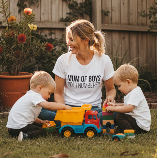 Mum of Boys #Outnumbered white t-shirt worn by mother sitting outdoors with two young boys playing with toy trucks