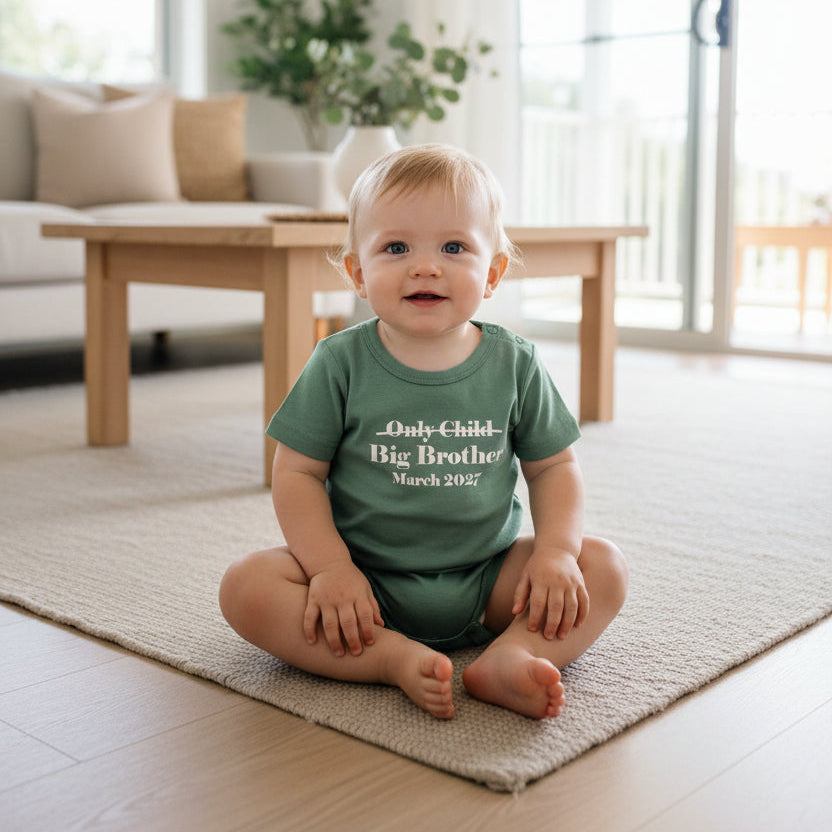 A sage green short-sleeve baby t-shirt with white printed text reading 'Only Child Big Brother March 2027' on the chest, displayed flat against a white background.