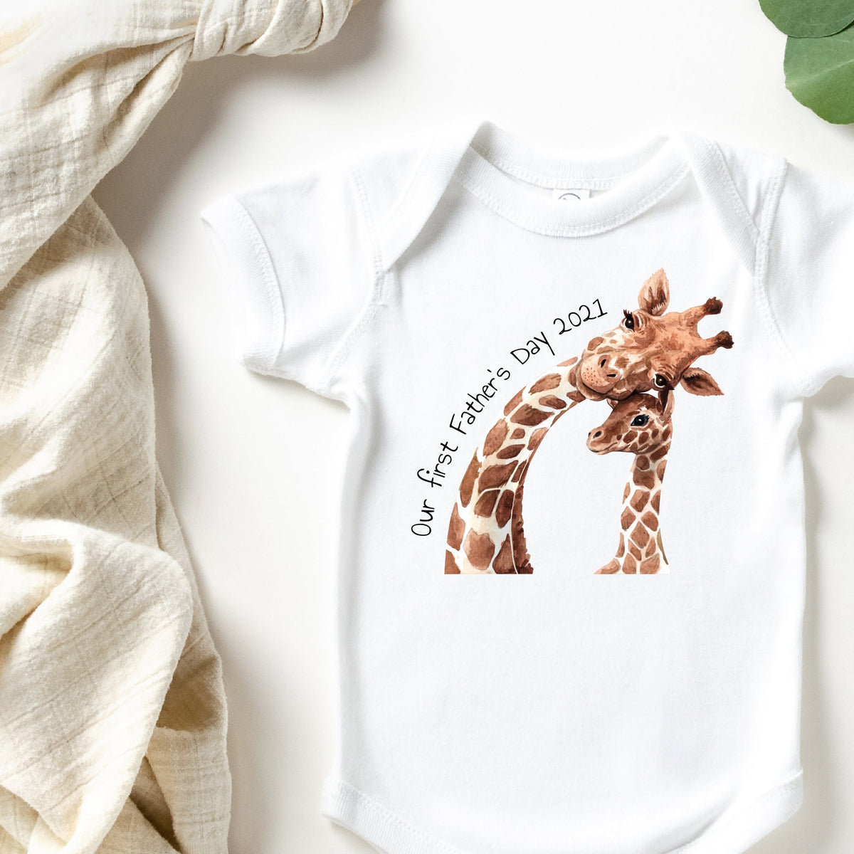 Dad and baby in matching white tops with a giraffe Our First Father's Day design, holding a giraffe toy.
