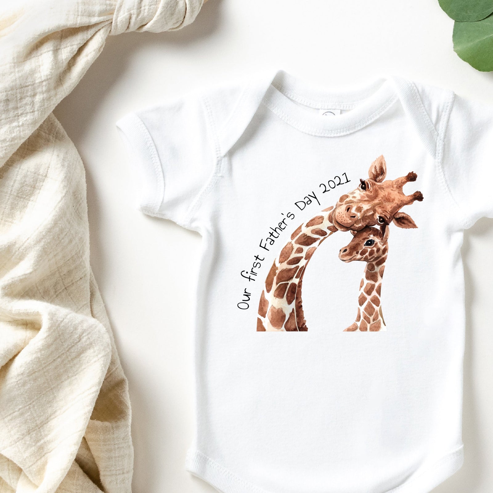Dad and baby in matching white tops with a giraffe Our First Father's Day design, holding a giraffe toy.
