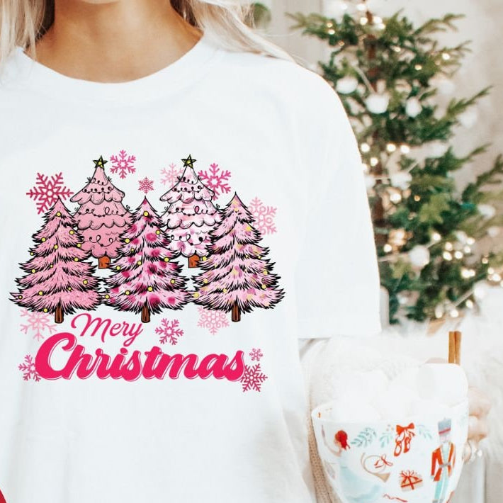 A woman holding a mug and wearing a white t-shirt with a Christmas tree and 'Merry Christmas' text design.