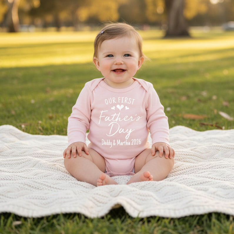 Pink long-sleeve baby bodysuit with Our First Father's Day and personalised names and year.