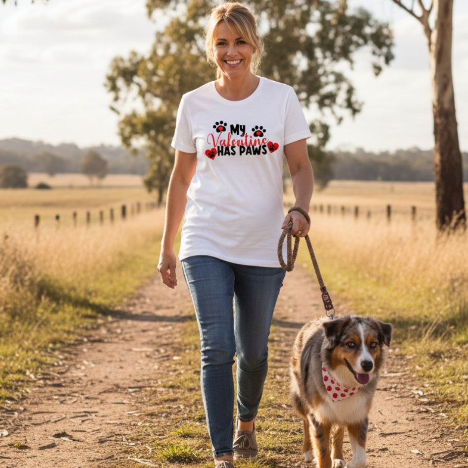 A white t-shirt with the text 'MY VALENTINE HAS PAWS' and a paw print symbol on it, presented next to a pair of blue denim jeans.